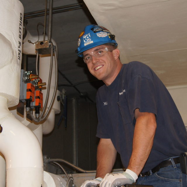 Worker fixing heating and air conditioning (HVAC) system to be more energy efficient.